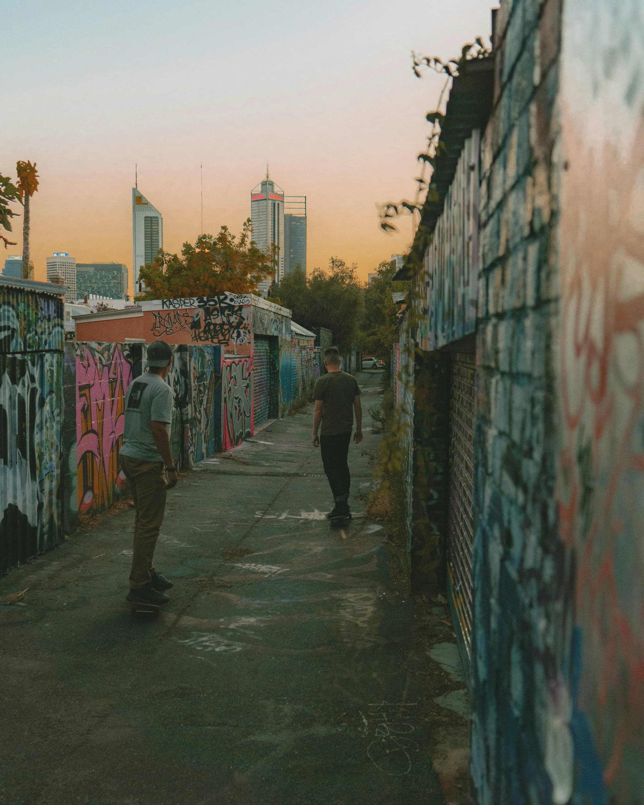 Skaters in a graffiti laneway against the city skyline at dusk